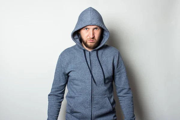 Young man in a hood with a serious, aggressive face on a light background.