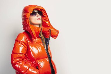 Kırmızı ceketli ve güneş gözlüklü mutlu bir genç kız hafif bir arkaplanda yukarı bakıyor. Gündelik moda, alışveriş, trend kavramı.