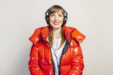 Kırmızı ceketli ve kulaklıklı mutlu genç kız hafif bir arka planda müzik dinliyor. Konsept müzik, moda, trend.