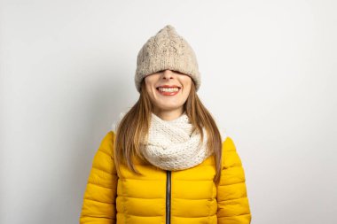 Genç bir kadın gözlerinin üstüne bir şapka, bir eşarp ve açık arkaplan üzerine sarı bir ceket giydi. Kış konsepti, kış modası, kış kıyafetleri.