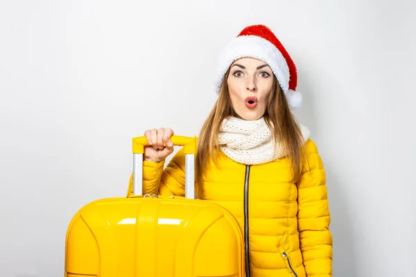 黄色のジャケットとサンタ クラスの帽子の若い女の子が黄色のスーツケースを持っています コンセプト新年 クリスマス — ストック写真