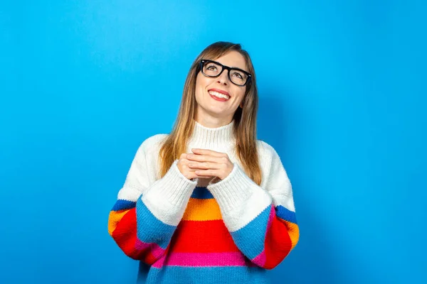 young girl with glasses and in a knitted sweater looks up, smiles, happy, dreams, ideas arose on a blue background. Banner.