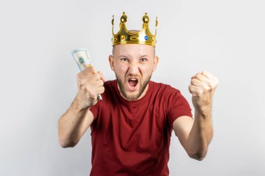 Altın tacın içindeki genç adam elinde para tutuyor ve arka planda zaferi kutluyor. Kavramsal kral, şans, kazanç, zenginlik, hayal, amaç, istek, bahis. Pankart.