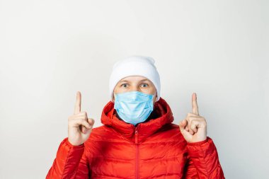 Tıbbi maskeli genç adam parmaklarını açık bir arkaplan üzerinde gösteriyor. Soğuk algınlığı, virüs, bulaşıcı hastalıklar.