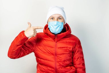 Genç adam arka planda yüzünde tıbbi bir maskeyi işaret ediyor. Soğuk algınlığı, virüs, bulaşıcı hastalıklar.