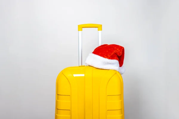 Yellow Plastic Suitcase Wearing Red Santa Claus Hat Light Background — Stock Photo, Image