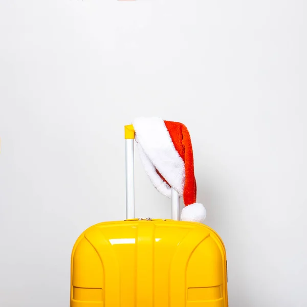 赤いサンタクロースの帽子をかぶった黄色のプラスチック製のスーツケースの上に光の背景 — ストック写真