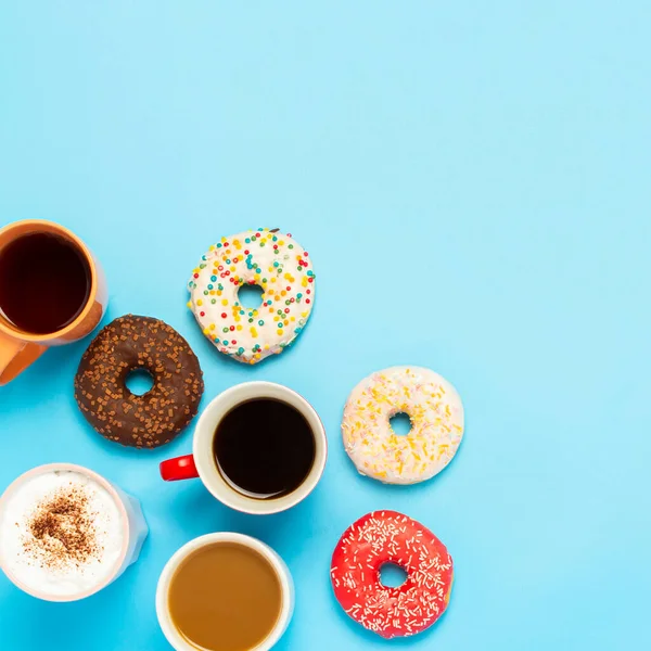 Tasty donuts and cups with hot drinks, coffee, cappuccino, tea on a blue background. Concept of sweets, bakery, pastries, coffee shop, meeting, friends, friendly team. square. Flat lay, top view.