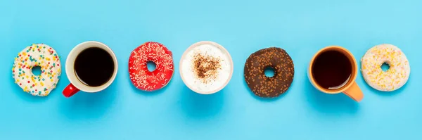 Tasty donuts and cups with hot drinks, coffee, cappuccino, tea on a blue background. Concept of sweets, bakery, pastries, coffee shop, meeting, friends, friendly team. Banner. Flat lay, top view.