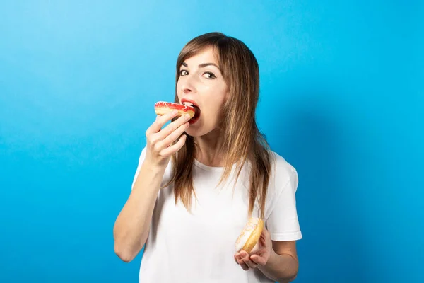 Genç Kız Donut Yiyor Mavi Arka Planda Iki Çörek Tutuyor — Stok fotoğraf