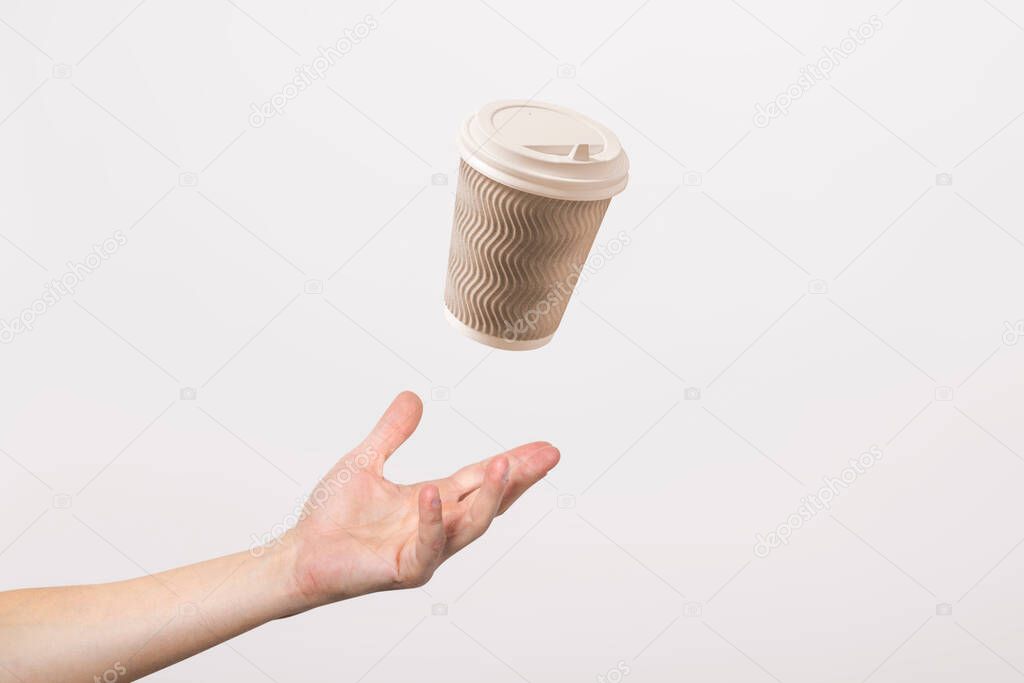 hand catches a cardboard glass on a light cardboard background. Concept of coffee, tea, advertising, coffee breaks.