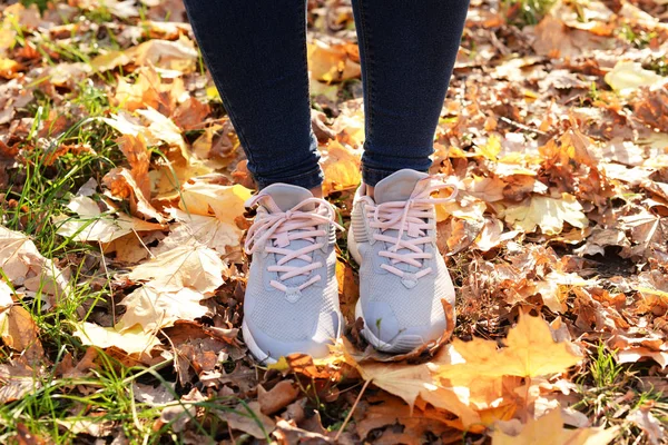 legs of the girl athlete who stands on the road in sneakers shoes for sports in yellow autumn leaves