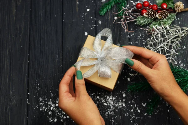 girl holds a surprise gift box with a bow on the background of branches of a Christmas tree ornaments on a wooden background