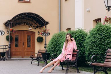 Pembe elbiseli genç, güzel bir kız şehirde dolaşıyor. Fotoğraf kapanışı ve genel plan. Bankta oturan kız.