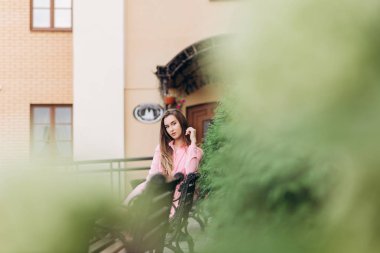 Pembe elbiseli genç, güzel bir kız şehirde dolaşıyor. Fotoğraf kapanışı ve genel plan. Bankta oturan kız.