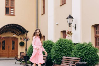 Pembe elbiseli genç, güzel bir kız şehirde dolaşıyor. Fotoğraf kapanışı ve genel plan. Bankta oturan kız.