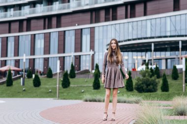 Genç bir kız omzunda bir çantayla ofisin yakınında yürüyor.