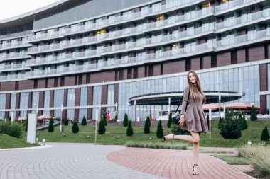 Genç bir kız omzunda bir çantayla ofisin yakınında yürüyor.