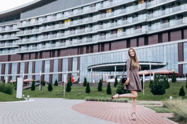 Genç bir kız omzunda bir çantayla ofisin yakınında yürüyor.