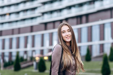 Genç bir kız omzunda bir çantayla ofisin yakınında yürüyor.