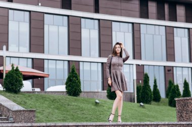 Genç bir kız omzunda bir çantayla ofisin yakınında yürüyor.