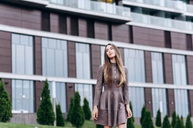 Genç bir kız omzunda bir çantayla ofisin yakınında yürüyor.