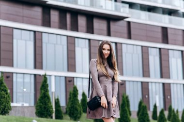 Genç bir kız omzunda bir çantayla ofisin yakınında yürüyor.