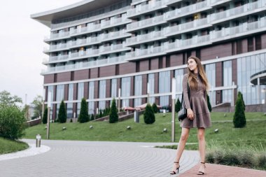 Genç bir kız omzunda bir çantayla ofisin yakınında yürüyor.