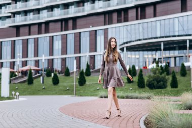 Genç bir kız omzunda bir çantayla ofisin yakınında yürüyor.