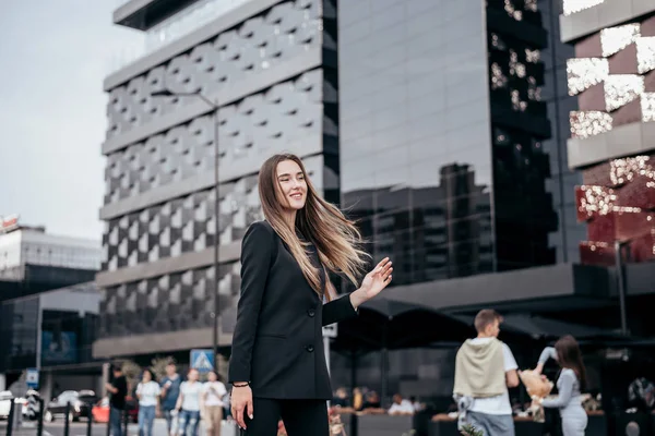 Young and attractive business girl on the background of the city in a beautiful black suit.