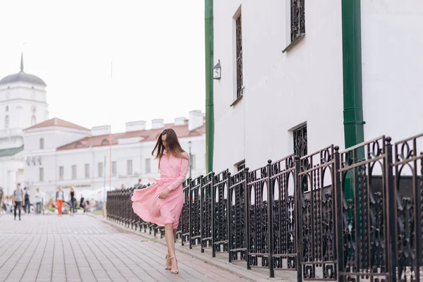 Ein junges, schönes Mädchen in einem rosa Kleid geht durch die Stadt. Foto aus nächster Nähe - und allgemeiner Plan. Mädchen sitzt auf einer Bank. — Stockfoto