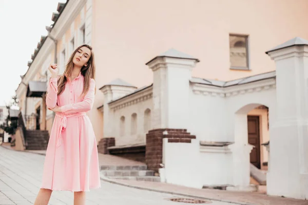 En ung, smuk pige i lyserød kjole går gennem de smukke gader i byen. Meget smukke portrætter af en pige i byen . - Stock-foto