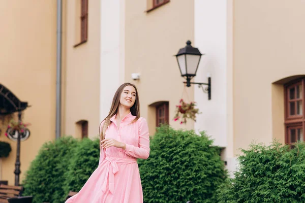 Uma jovem, linda menina em um vestido rosa caminha pela cidade. Foto de perto - para cima e plano geral. Menina sentada em um banco . — Fotografia de Stock