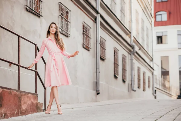 En ung, vacker flicka i rosa klänning går genom de vackra gatorna i staden. Mycket vackra porträtt av en flicka i staden. — Stockfoto