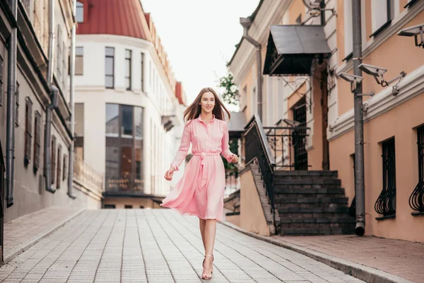 A young, beautiful girl in a pink dress walks through the beautiful streets in the city. Very beautiful portraits of a girl in the city. — Stock Photo, Image