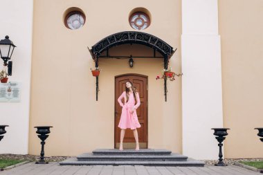 Pembe elbiseli genç, güzel bir kız şehirde dolaşıyor. Fotoğraf kapanışı ve genel plan. Bankta oturan kız.