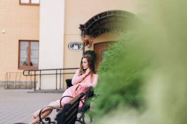 Pembe elbiseli genç, güzel bir kız şehirde dolaşıyor. Fotoğraf kapanışı ve genel plan. Bankta oturan kız.