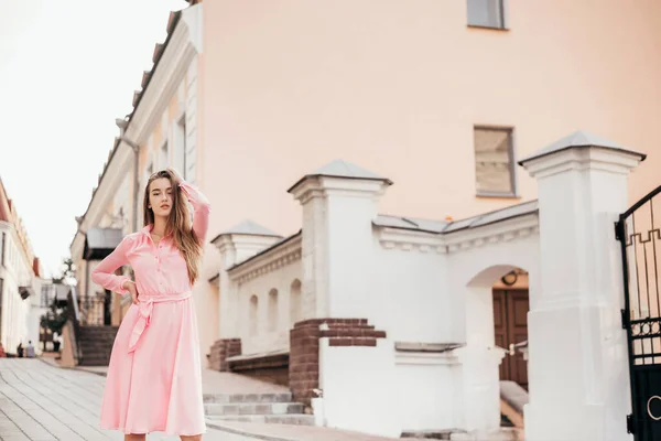 Una chica joven y hermosa con un vestido rosa camina por las hermosas calles de la ciudad. Retratos muy bonitos de una chica en la ciudad . — Foto de Stock