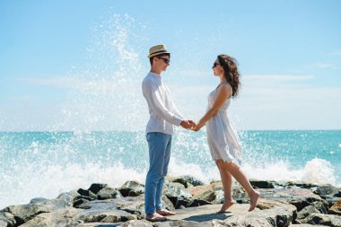 Bir çift genç aşık, bir adam ve bir kız okyanusta, taşların üzerinde beyaz elbiseler içinde.