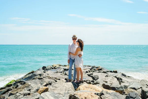Et ungt par elskere, en fyr og en jente på havet, i hvite klær på steinene. – stockfoto