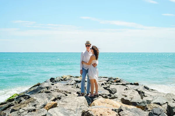 A young couple of lovers, a guy and a girl on the ocean, in white clothes on the stones. — Stock Photo, Image