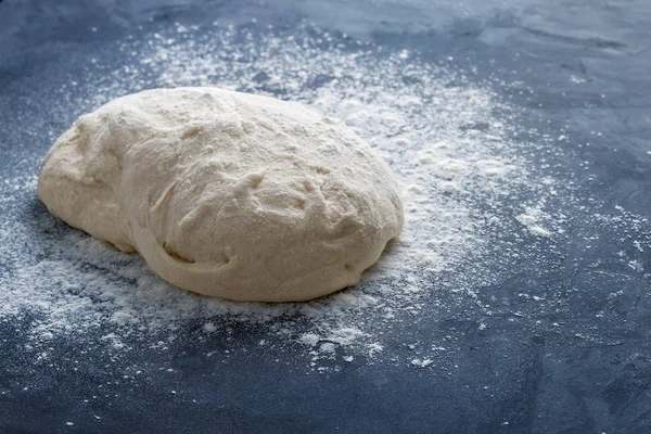 Çiğ maya pişirme hamuru bir top ve dokulu mavi beton arka plan üzerine beyaz buğday unu serpilir. Yakın çekim, yan görünüm