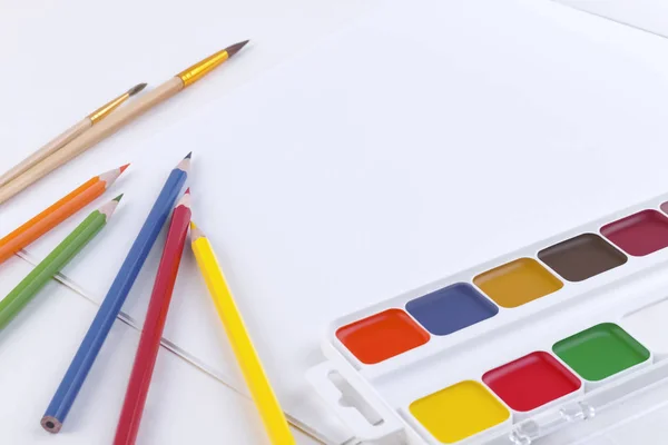明亮的水彩颜料、彩色铅笔、用于绘图的画笔和带有空白页面的开放式相册的明亮水彩画、彩色铅笔和打开的相册的侧视图，用于白色桌子上的文本 — 图库照片