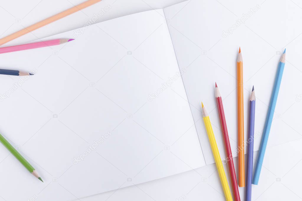 Beautiful designer composition with a group of scattered colored wooden pencils and an open sketchbook with empty pages for text, picture or other design element