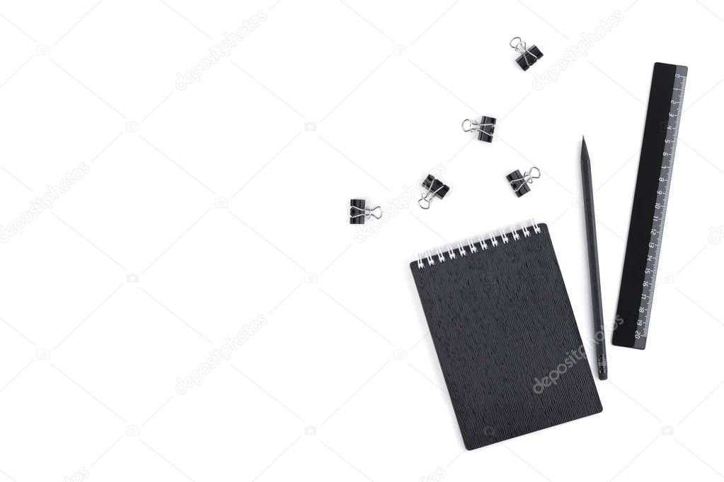 Top view on notepad with black cover, black glossy plastic ruler, wooden pencil and stationery clips with empty place for text isolated on white background