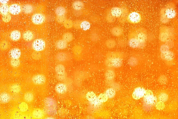 Krople wody na szklankę z pomarańczowym, żółtym, złotym bokeh koła świetlne wyglądają jak piwo lub szampan w szklanym zbliżeniu. Streszczenie jasnych Świąt, tło Nowego Roku. Koncepcja reklamowa lub wakacyjna — Zdjęcie stockowe