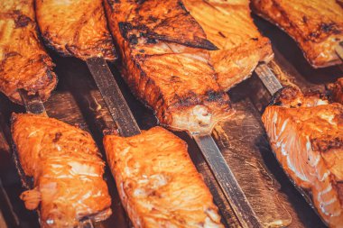 Meyve pazarında sığ bir tarla derinliği olan metal şişler üzerinde yağlı, kızarmış kırmızı balık parçalarını kapatın. Şehrin turistik bölgesinde sokak yiyeceği. Kömür ızgarasında pişmiş kırmızı balık..
