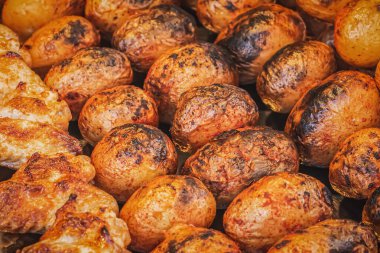 Altın hamura pişirilmiş bir patatesin yan görüntüsü. Sokak pazarında kömür ızgarasında şiş üstünde patates kızartması. Lezzetli fırında patates ve sığ bir tarla derinliğinde baharatlar.