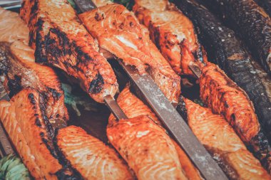 Kömür ızgarasında pişirilmiş şiş somon bifteği. Sokak tezgahında ızgarada kızartılmış kırmızı balık. Yüzeyde sığ derinlikte pişmiş balığın yan görüntüsü