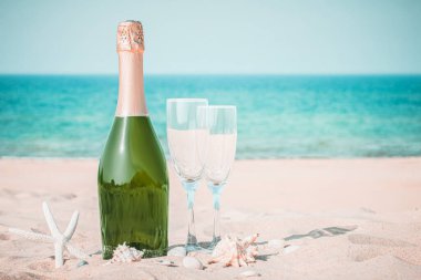 Bir şişe şampanya ve kumsalda iki bardak deniz kabuğu ve tropik bir plajda. Kopyalama alanı olan şablon